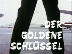 title card : DER GOLDENE SCHLüSSEL superimposed on the villain’s legs framing Emma driving away from the airport