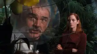 Sir August and Mrs. Peel look at his prize orchid, Sir August’s face massively enlarged by the magnifying disc in front of it