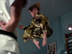 Low-angle shot of Purdey leaping into the air in her gold silk karate gi