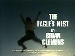 title card: white all caps text reading ‘THE EAGLE’S NEST BY BRIAN CLEMENS’ superimposed on a freeze frame of Stannard leaping off the cliff, arms and legs outstretched