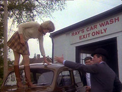 Purdey stands on top of the Plymouth at the exit of Ray’s Car Wash, her long skirt shrunken by the carwash down to a miniskirt length; Steed offers her a hand to help her down