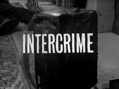 title card: white all caps text reading ‘INTERCRIME’ superimposed on a close-up of an up-turned case, the feet of a dead body in view behind it