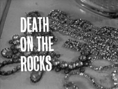 title card: white all caps text reading ‘DEATH ON THE ROCKS’ superimposed on jewellery lying on a dressing table