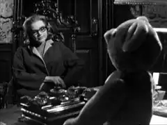 Cathy, wearing spectacles, has an interview with a teddy bear