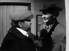 Mr. Teddy Bear, disguised as a technician, greets Steed as they pass each other in Steed’s doorway