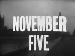 title card: white all caps text reading ‘NOVEMBER FIVE’ superimposed on a shot across Westminster Bridge towards the Houses of Parliament and Big Ben