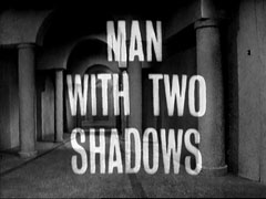 title card: white all caps text reading ‘MAN WITH TWO SHADOWS’ superimposed on a view up a vaulted corridor - probably a model