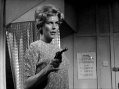 Cathy, wearing a gold lamé pullover, wields her hefty revolver in Steed’s cabin