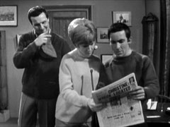 Ann and Lynton read the newspaper headline while Steed looks on, rubbing his chin
