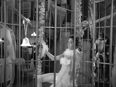 Mrs. Peel is singularly unimpressed with being locked in a cage wearing a bodystocking and a few feathers, Auntie gloats from behind the cage