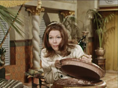 Mrs. Peel lidts the lid of a huge jar to see if the missing corpse is there
