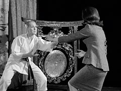 Mrs. Peel has removed her shoes but kept her tight suit on to spar with Oyuka who more sensibly wears a karate gi. A ceremonial gong stands at the back of the dojo