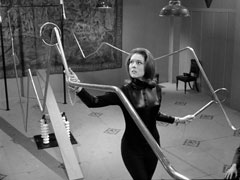 Mrs. Peel, in a stretch catsuit, is midway through her initiation test, risking her life on an electrified obstable course