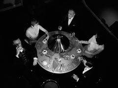 An overhead view of the Boardman’s coffee table, showing that it’s designed to look like an old coin. Steed, Mrs. Boardman, Mr. Boardman, Mrs. Peel, and Harvey sit around it