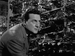 Steed crouches behind a wine rack as he hunts down Harvey in the cellar