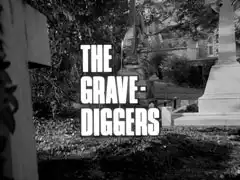 title card: white all caps text reading ‘THE GRAVE- DIGGERS’, outlined in black, superimposed on a view of the graveyeard, ivy creeping over the cross nearest us