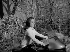 Mrs. Peel declares Steed a fraud as he closes the sidecar while she kicks the starter of the motorcycle