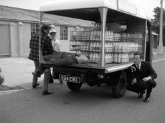 Steed crouches behind the milk float as another inert RAF officer is loaded onto it by the crooks