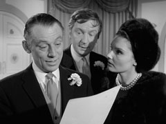 Lovejoy, on the left, smiles at Mrs. Peel’s photo as Barabara tells him Mrs. Peel was at Henshaw’s apartment. Dinsford, standing between them, looks worried