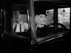 Emma chauffeurs the hearse while Steed gets dressed in the back