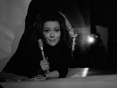 Mrs. Peel smiles through the torn film screen after defeating Holly Trent