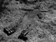 Eli’s boots lie at the feet of a man-shaped pool of water in the soggy field