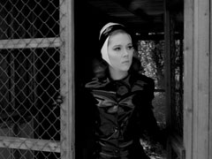 Mrs. Peel emerges from a hut dressed is a very tight PVC mack and black and white rubber hat