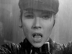 Close-up of Mrs. Peel during the fight in the rainstorm; water pours off her cap and hair and she is thoroughly wet