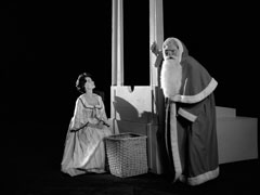 Madame Guillotine kneels before the guillotine alongside the evil Santa, who holds the rope that will make the blade fall
