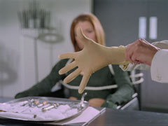 Dr. Voss pulls on a surgical glove as she prepares to subject Mrs. Peel to the base fear - pain