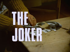 title card: white all caps text with black dropshadow to the left reading ‘THE JOKER’ superimposed on someone wearing a mustard jumper cutting up Emma’s photo with a pair of scissors