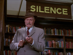 Williams, his revolver drawn, fits a silencer to it in response to the sign requesting SILENCE in the library