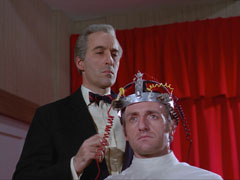 Dr. Penrose’s duplicate is strapped to the brain transfuser by Professor Stone to have his memory is drained, the red curtain behind accentuates the drama of the scene.