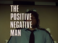 title card: white all caps text outlined in black reading ‘THE POSITIVE NEGATIVE MAN’ superimposed on Dr. Grey embedded in the plaster of the wall