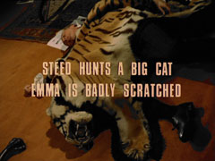 subtitle card: white all caps text with black dropshadow to the left reading ‘STEED HUNTS A BIG CAT
			EMMA IS BADLY SCRATCHED’ superimposed on a tiger skin lying over Williams’ contorted body