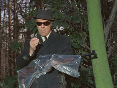 Earle holds Flanders’ rifle, wrapped in plastic, preparing to assassinate Scott