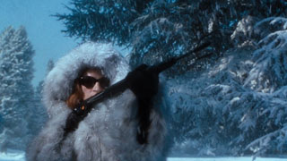Evil Emma, in her fur coat, fires a black spear gun at Steed who is off-camera
