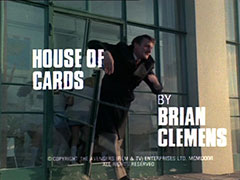 title card: white all caps text reading ‘HOUSE OF CARDS BY BRIAN CLEMENS’ superimposed on Perov crashing through the glass door trying to catch his quarry