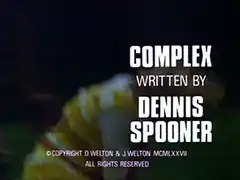 title card: white all caps text reading ‘COMPLEX 
			WRITTEN BY
			DENNIS
			SPOONER’ superimposed on an out of focus close-up shot of Purdey running across a field at night, about to bend down