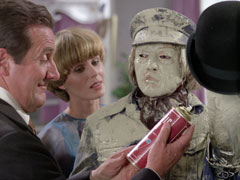 Steed looks at his can of aerosol plastic skin before Kane’s frozen face, Purdey looks on over Kane’s right shoulder