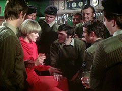 Purdey, in a fetching red dress and matching tights, sits in the middle of the pub surrounded by uniformed soldiers, one of whom has put a hand on her knee