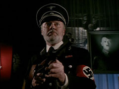 Trasker, now in full Gestapo uniform, aims his submachinegun