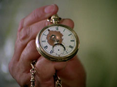 Steed holds up the pocket watch that saved his life, the face smashed and marked by the bullet