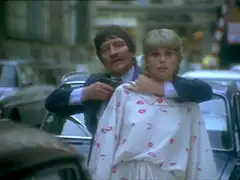 The embassy guard puts his arm around Purdey’s throat, using her as a shield and pointing his gun at her, threatening to shoot her unless Gambit lets him escape