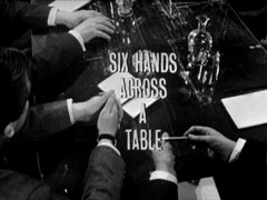 title card: white all caps text reading ‘SIX HANDS ACROSS A TABLE’ superimposed on ... well, on six hands across a table