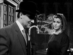 Steed, in bowler hat, umbrella and suit, asks the receptionist to tell Sir Charles he called