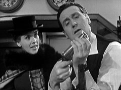 Steed examines the consignment of arms he’d forgotten to cancel while Cathy looks on, bemused