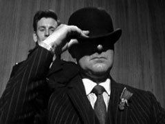 In court: Steed demonstrates that the bowler hat found at the crime scene is far too big for him - his head disappearing into it
