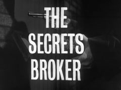 title card: white all caps text reading ‘THE SECRETS BROKER’ superimposed on a dark close-up of Paignton taking the revolver from the box
