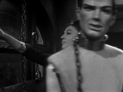 Madge reaches behind a mannequin wearing an iron collar and chains